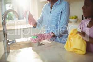 Mother assisting her daughter in cleaning utensils