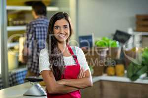Smiling woman vendor standing at the counter in grocery store with arms crossed