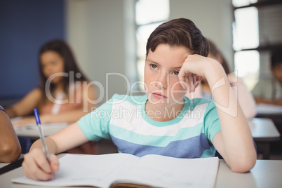 Tensed school boy doing homework in classroom