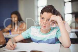 Tensed school boy doing homework in classroom