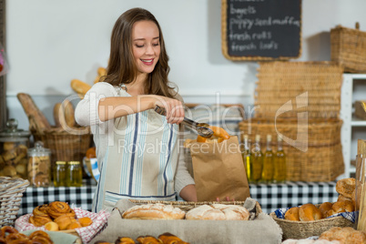 Smiling female staff putting croissant into a paper bag at counter