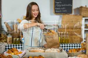 Smiling female staff putting croissant into a paper bag at counter