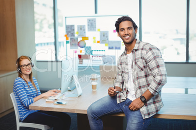 Male graphic designer sitting on desk with coworker in conference room