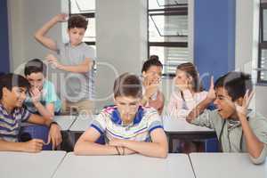 School friends bullying a sad boy in classroom