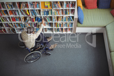 Overhead view of disabled school teacher selecting book in library