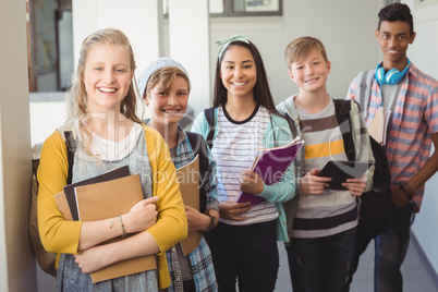 Group of smiling students standing with notebook in corridor