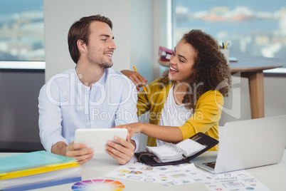 Smiling graphic designers sitting at table and using digital tablet