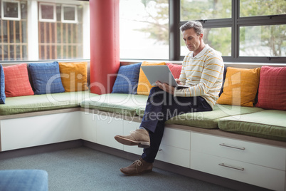 Attentive school teacher using laptop in library