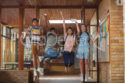 Excited classmates jumping with grade cards in corridor