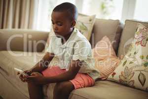 Boy sitting on sofa and using mobile phone in living room