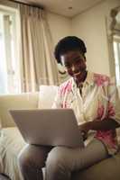 Portrait of woman sitting on sofa and using laptop in living room