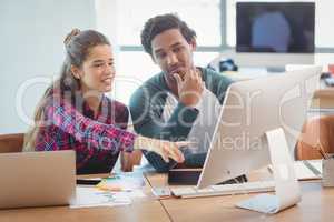 Male and female graphic designers discussing over computer