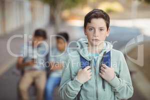 Portrait of sad schoolboy with schoolbag standing in campus