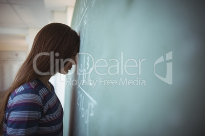 Tired schoolgirl standing with closed eyes near chalkboard in classroom