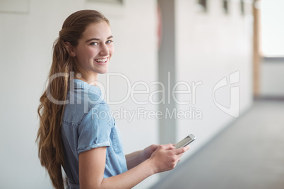 Portrait of happy schoolgirl using mobile phone in corridor