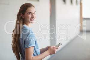 Portrait of happy schoolgirl using mobile phone in corridor
