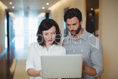 Male and female business executives using laptop in corridor Male and female business executives using laptop in corridor