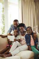 Parents and son using digital tablet on sofa in living room