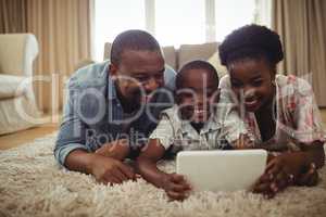 Parents and son using digital tablet while lying on a rug