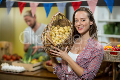 Smiling woman vendor holding a basket if potatoes in grocery store