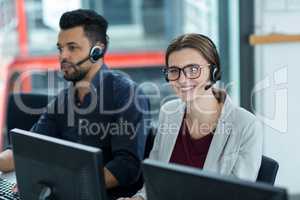 Business executives with headsets using computers at desk in office