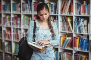 Attentive schoolgirl reading book in library