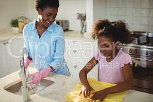 Mother assisting her daughter in cleaning utensils