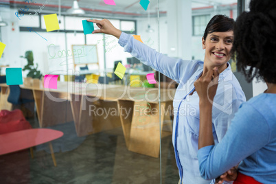 Female graphic designer pointing to the sticky notes on the glass in creative office