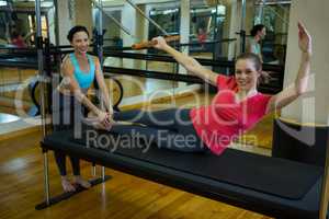 Portrait of female trainer assisting woman with stretching exercise on reformer