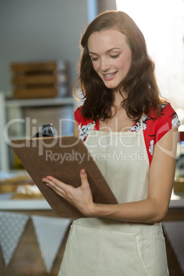 Female shop assistant writing on the clipboard at the counter