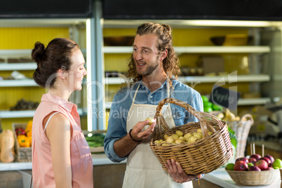 Smiling vendor holding a basket of potatoes while interacting with woman