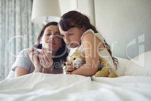Mother showing temperature on thermometer to her daughter