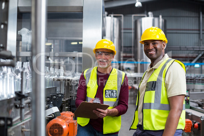 Two factory workers discussing while monitoring drinks production line