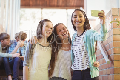 Smiling schoolgirls taking selfie with mobile phone in corridor