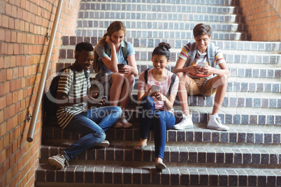 Classmates sitting on staircase and using mobile phone