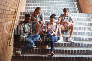 Classmates sitting on staircase and using mobile phone