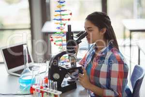 Attentive schoolgirl looking through microscope in laboratory