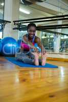 Portrait of smiling fit woman doing stretching exercise on mat
