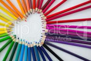 Colored pencils arranged in heart shape on white background