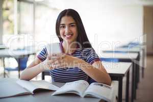 Portrait of schoolgirl using mobile phone while studying in classroom