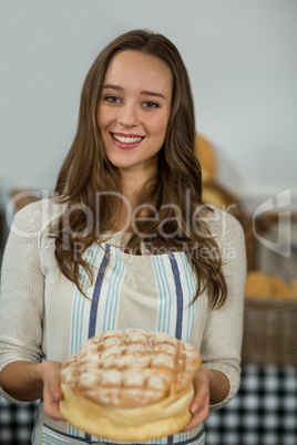 Portrait of smiling female staff offering round loaf of bread at counter