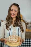 Portrait of smiling female staff offering round loaf of bread at counter
