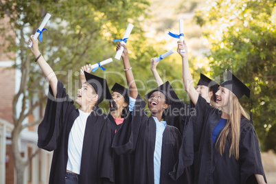 Smiling graduate school kids standing with degree scroll in campus