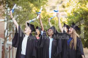 Smiling graduate school kids standing with degree scroll in campus