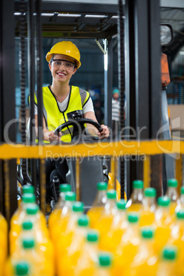 Female factory worker loading packed juice bottles on forklift in factory