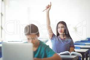 Attentive schoolgirl raising hand in classroom