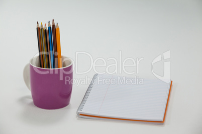 Colored pencils kept in cup and notepad