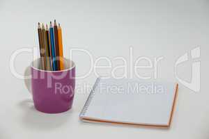 Colored pencils kept in cup and notepad