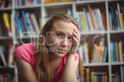 Portrait of sad schoolgirl sitting in library