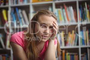 Portrait of sad schoolgirl sitting in library